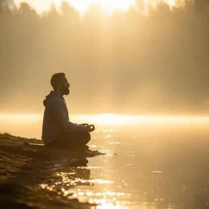 Person meditating alone by calm water at sunrise